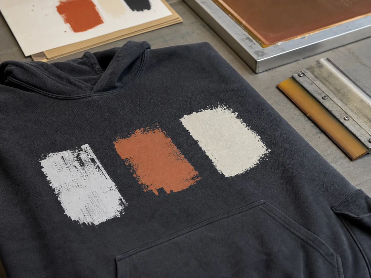 Abstract ink tests on an unbranded hoodie panel beside print-development tools.