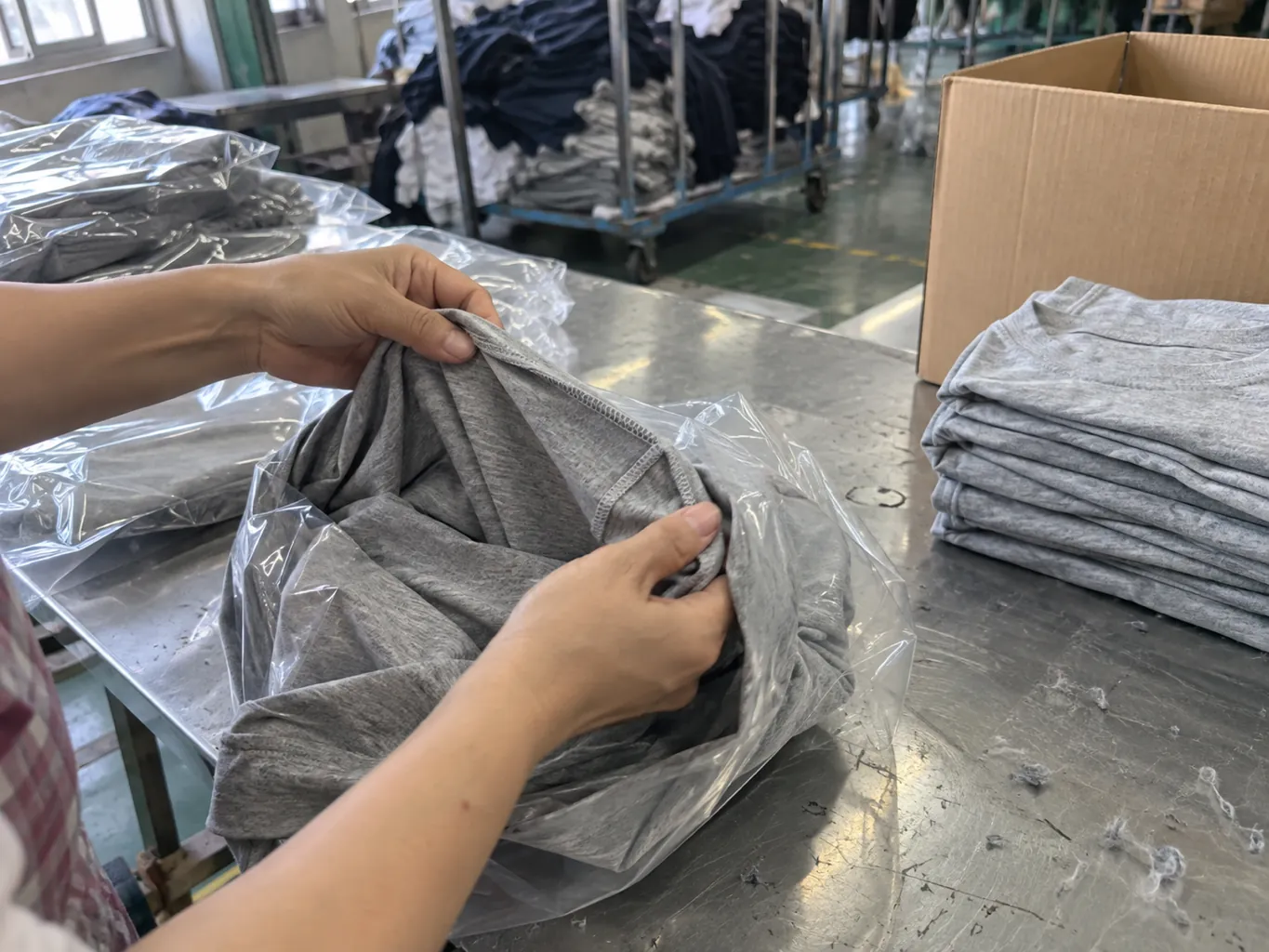 Hands turning a finished shirt inside out to inspect a seam beside a packing carton