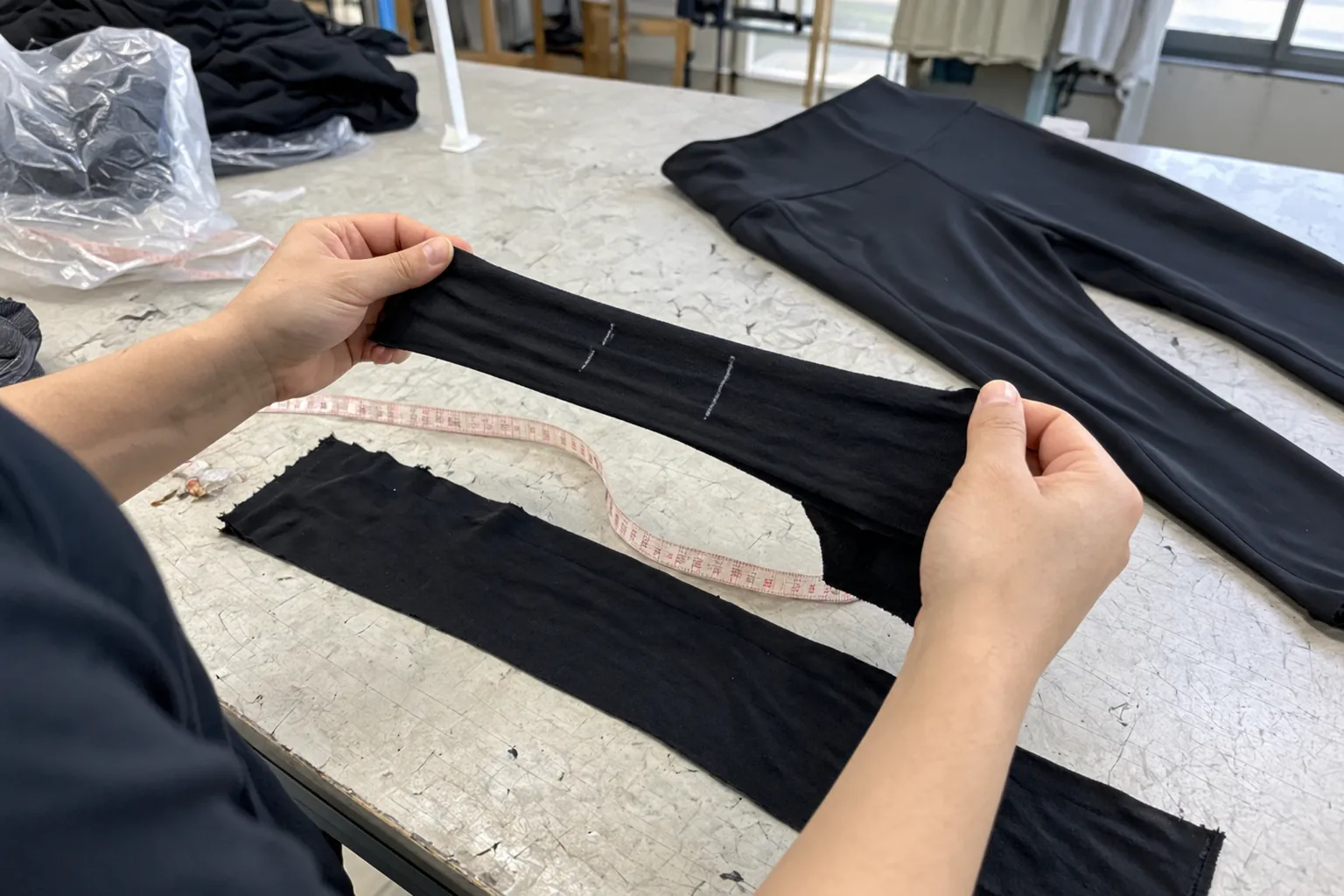Manos estirando una tira de tejido elástico negro con marcas de tiza y cinta métrica