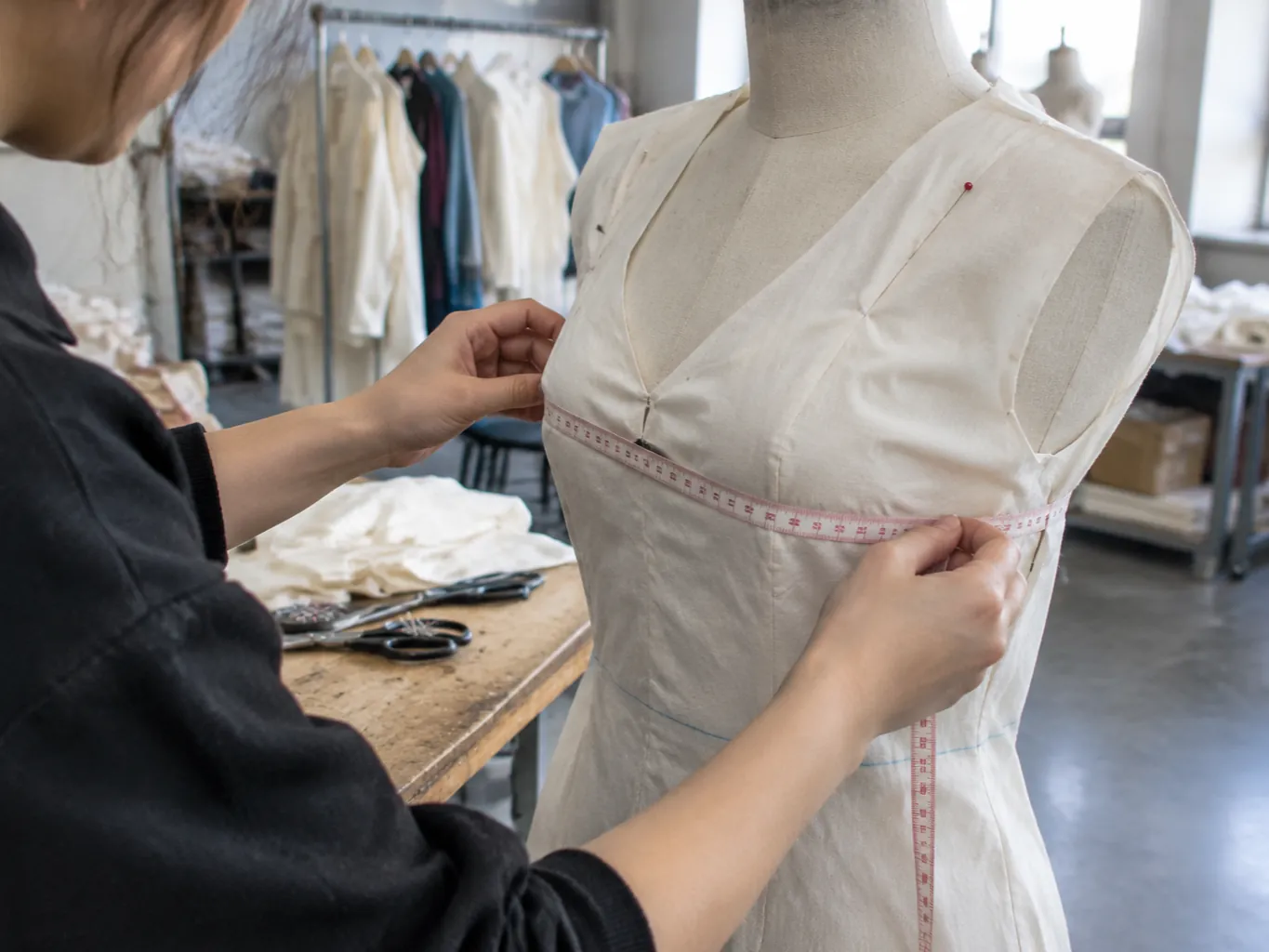 Mains ajustant un mètre ruban sur le buste d'un mannequin portant une toile