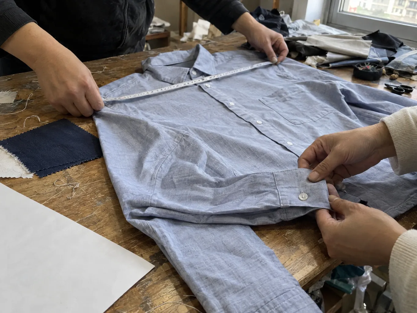Des mains mesurent un échantillon de chemise et inspectent la couture de son poignet.
