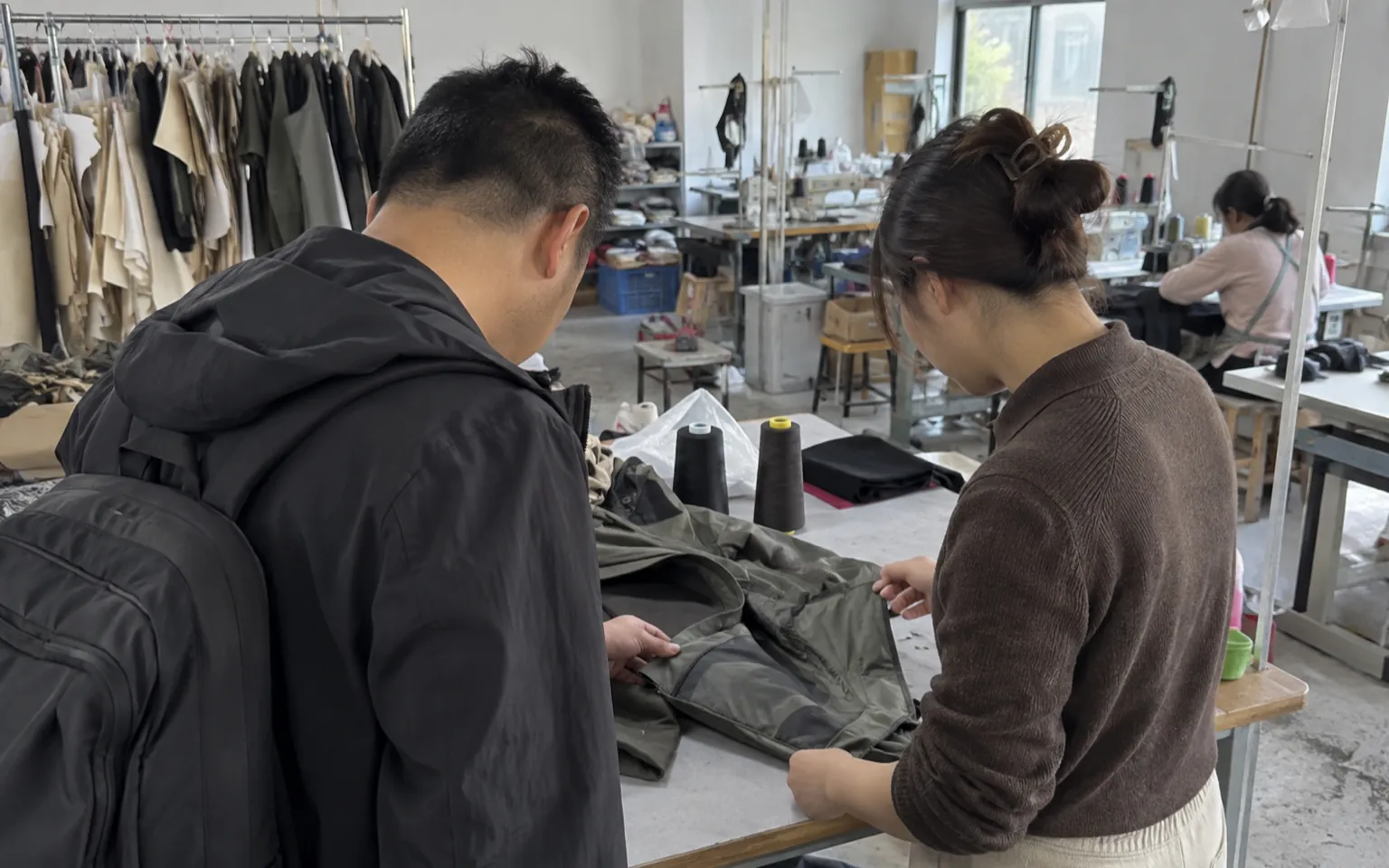 Deux personnes inspectent un échantillon de veste sur une table d’atelier.